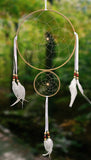 Large 8" diameter ring and smaller 4" ring wrapped in tan leather and adorned with white satin and feathers accented with brick red and beige wooden beads on dark green blurred background