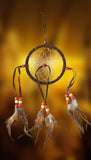 4-3/8" diameter ring wrapped in chocolate brown leather with chocolate brown leather straps and brown & white feathers and brick red and beige wooden beads on golden background.