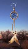 2" diameter ring wrapped in tan leather and adorned with leather straps and brown & white feathers. Accented with brown and beige wooden beads on blue sky background.. 
