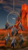 A 6-1/2" diameter ring wrapped in tan leather with tan leather straps and earth-toned feathers accented with brick red and beige wooden beads on a blurred western landscape.