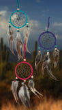 A dream catcher set iof three colors: Red, Blue, & Teal, and are adorned with complimentary beads and brown/gray feathers.